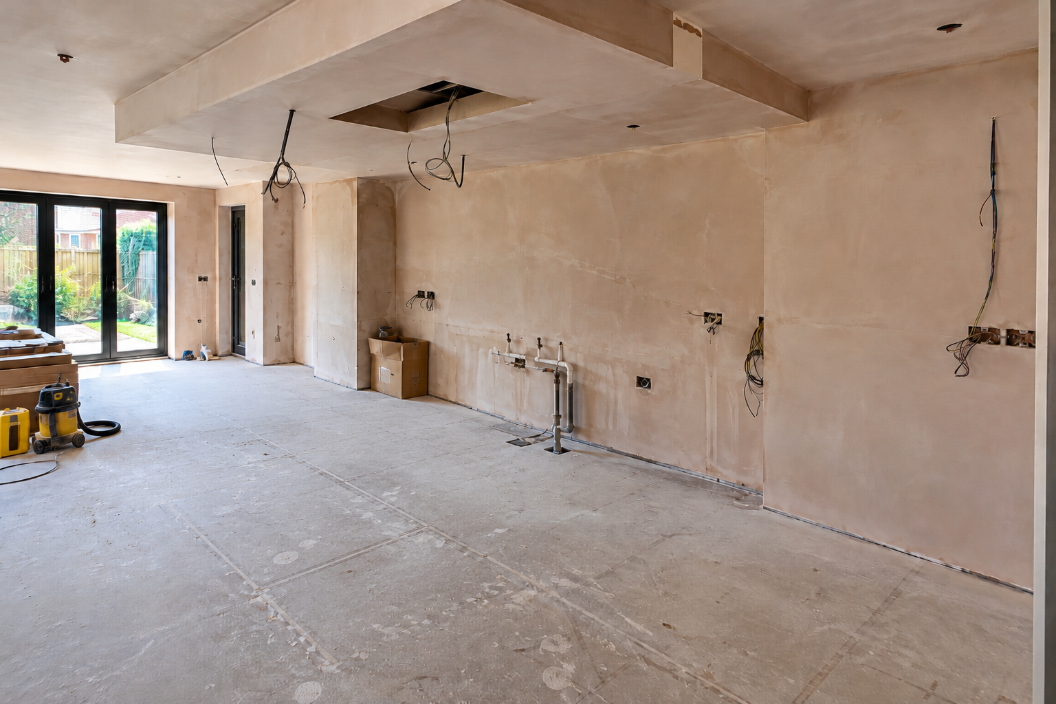 Kitchen renovation before installation showing an empty room with plastered walls, exposed plumbing and electrical wiring